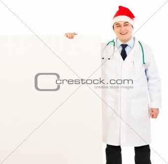 Smiling medical doctor in Santa hat holding blank billboard
