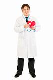 Smiling doctor holding stethoscope on paper heart 
