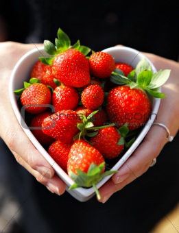 strawberries in heart shape bowl with hands