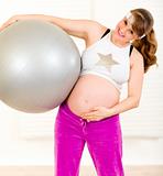 Smiling beautiful pregnant woman holding fitness ball and touching her belly
