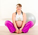 Smiling beautiful pregnant woman doing stretching exercises at home
