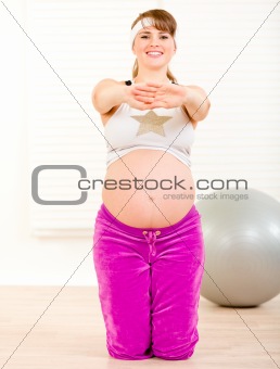 Smiling beautiful pregnant woman doing fitness exercises at living room
