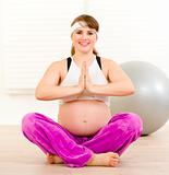 Smiling beautiful pregnant woman doing yoga exercises on floor at home
