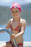 Little child in bathing cap, glasses on the swimming pool stairs