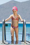 Little girl in bathing cap, glasses walks up the swimming pool s