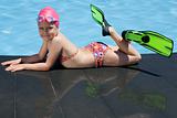 Little child in bathing cap, glasses, fins near swimming pool 