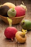 Group ripe variegated radishes in woven bowl on board