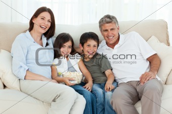 Family watching tv while they are eating popcorn