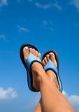 female legs with flip-flops over blue sky