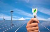 eco power concept.hand holding green power plug and solar panel and wind turbine background