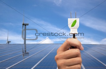 eco power concept.hand holding green power plug and solar panel and wind turbine background