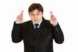 Superstitious young businessman holding crossed fingers
