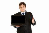 Smiling  businessman holding laptops blank screen and showing  thumbs up gesture
