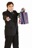 Smiling young businessman with shopping bags giving credit card
