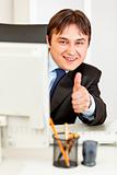 Smiling  businessman looking from monitor and showing thumbs up gesture
