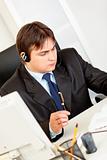 Serious businessman with  headset sitting at office desk and checking timetable in diary
