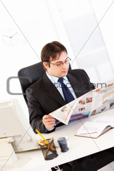 Modern businessman  sitting at office desk and reading newspaper

