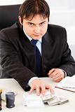 Concentrated businessman  sitting at office desk and giving money packs
