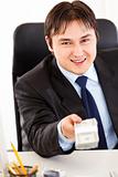 Smiling  businessman sitting at office desk and giving dollar pack
