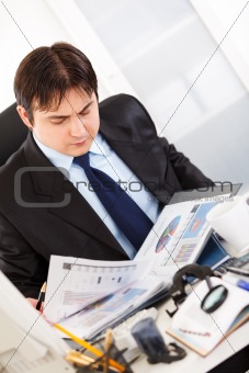  Serious businessman sitting at office desk and working  with financial documents
