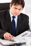  Serious businessman sitting at office desk and checking financial report
