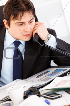 Concentrated businessman sitting at office desk and talking on phone
