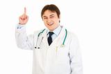 Smiling young medical doctor pointing finger up
