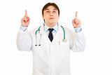 Smiling young medical doctor pointing fingers up

