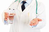 Medical doctor with pill and glass of water in hands. Close-up.
