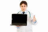 Medical doctor holding laptops with blank screen and showing  thumbs up gesture
