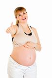 Smiling pregnant woman touching her belly and showing  thumbs up gesture
