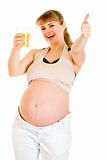 Smiling pregnant woman holding glass of juice and showing  thumbs up gesture
