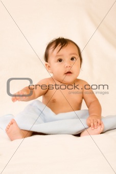 Excited ethnic baby boy sitting on blanket
