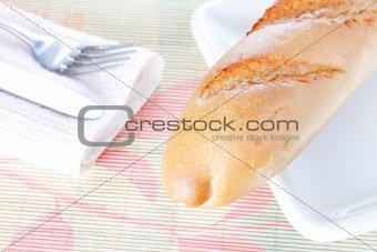 Baguette on white plate, napkin, fork and knife