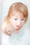 boy with long blong hair standing in bathtub looking up