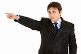 Serious young businessman pointing finger in corner
