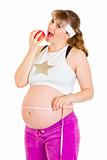 Smiling beautiful pregnant woman holding measure tape and  eating apple
