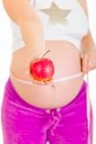 Pregnant woman measuring her belly and holding apple. Close-up.
