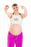 Smiling beautiful pregnant woman pointing finger at measure tape and  apple
