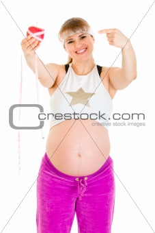 Smiling beautiful pregnant woman pointing finger at measure tape and  apple
