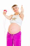 Smiling beautiful pregnant woman with measure tape and apple showing thumbs up gesture
