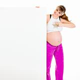 Smiling beautiful pregnant woman pointing finger at blank billboard
