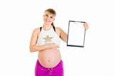 Smiling beautiful pregnant woman pointing on blank clipboard
