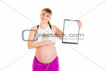Smiling beautiful pregnant woman pointing on blank clipboard
