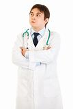 Thoughtful doctor with crossed arms on chest looking up at copy space
