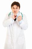 Angry  medical doctor with finger at mouth and threaten with fist
