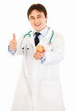 Smiling  medical doctor holding apple and showing thumbs up gesture
