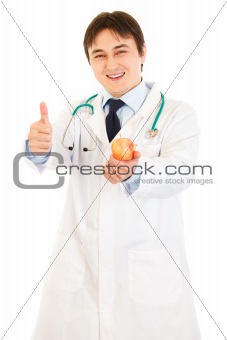 Smiling  medical doctor holding apple and showing thumbs up gesture
