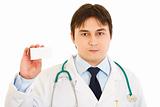 Serious medical doctor holding  blank business card in hand
