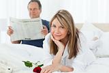 Happy woman with her rose while her husband is reading a newspaper